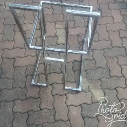 A pair of bare mild steel stool frames laid on paving, showing the repeated cantilever geometry