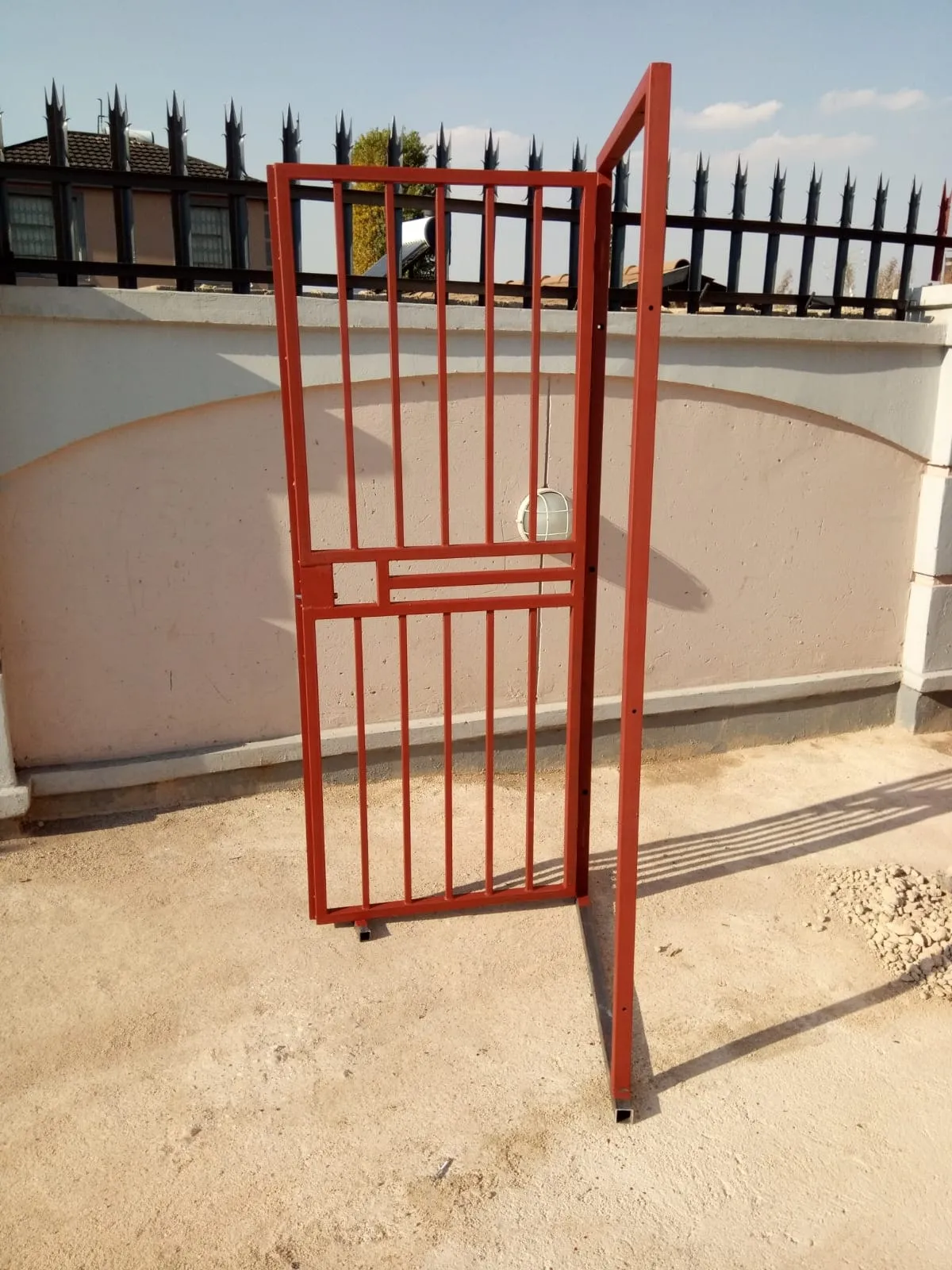 Mild steel pedestrian gate in red-oxide primer, hung in its frame against a garden wall