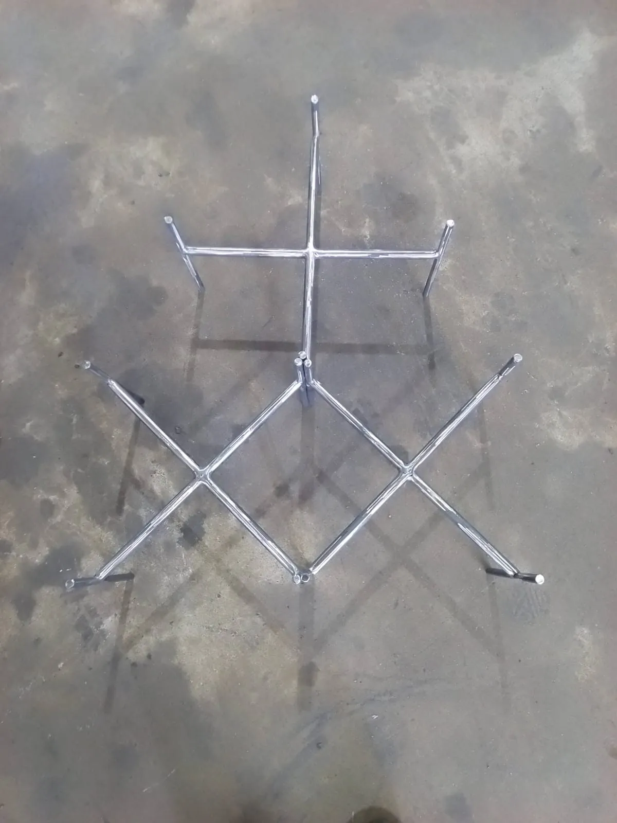 Cross-braced mild steel table base laid flat on the workshop floor, showing the welded centre joint